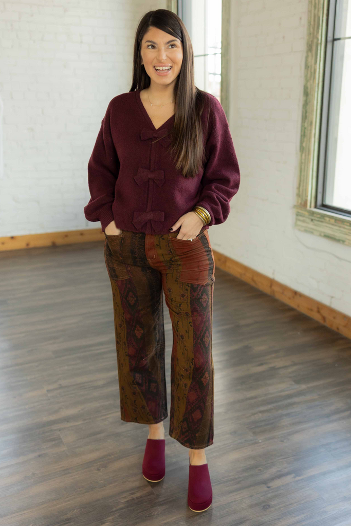 Kayla wearing the Ava burgundy knit pullover sweater with bow details down the front, paired with printed patchwork pants
