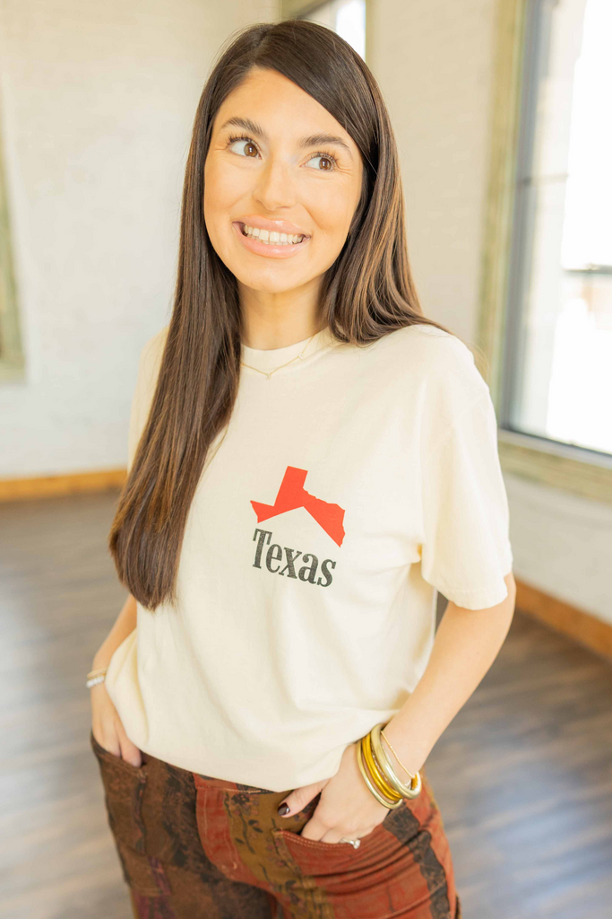 Kayla wearing the Texas Cowboy Icon graphic tee in cream with red Texas print on front and cowboy graphic on back, styled with printed pants inside Ruby and Yaya’s studio.