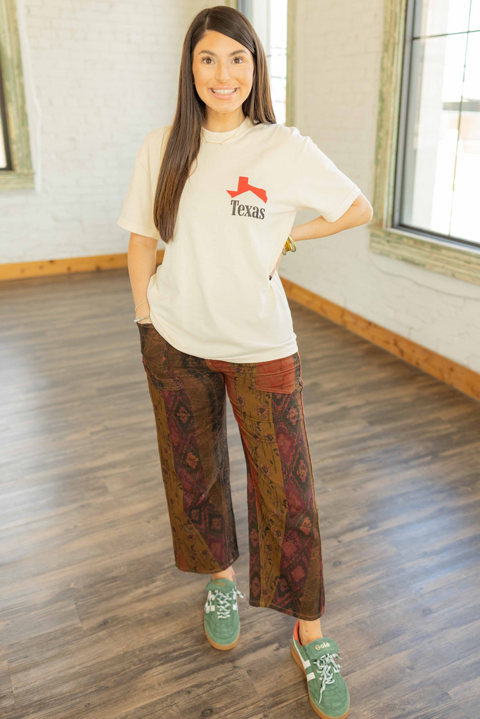 Kayla wearing the Texas Cowboy Icon graphic tee in cream with red Texas print on front and cowboy graphic on back, styled with printed pants inside Ruby and Yaya’s studio.