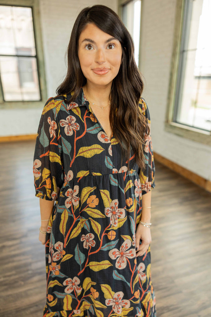 Kayla wearing the Reagan Floral Pullover Midi Dress, a charcoal 3/4 sleeve tiered midi dress with rust, mustard, and olive floral print, styled with burgundy pointed toe heels.