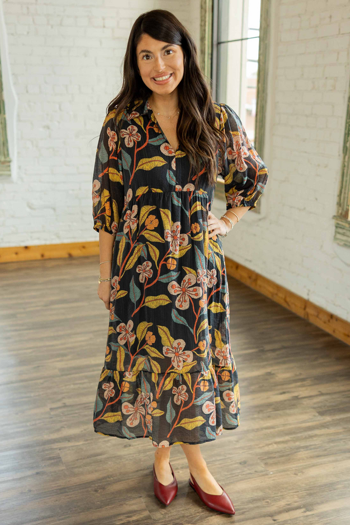 Kayla wearing the Reagan Floral Pullover Midi Dress, a charcoal 3/4 sleeve tiered midi dress with rust, mustard, and olive floral print, styled with burgundy pointed toe heels.