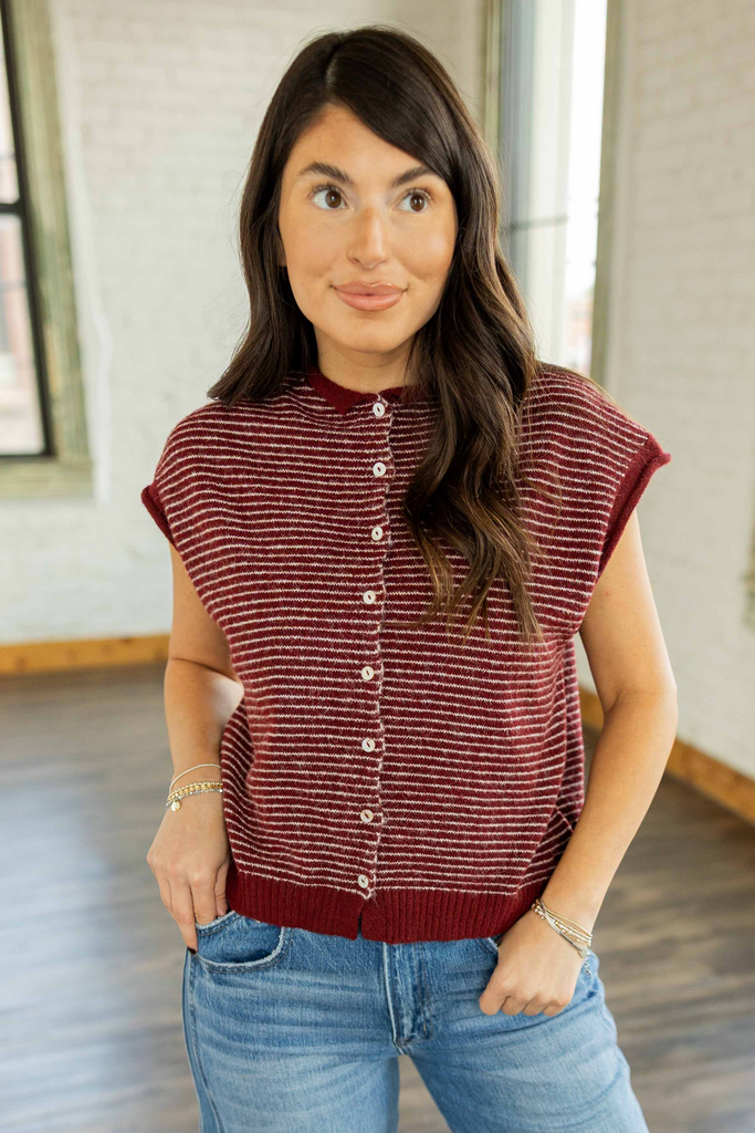 Kayla wearing the Imani Striped Sweater Vest Top, a maroon and cream striped knit vest with a button front and cap sleeves, styled with light wash wide leg jeans.