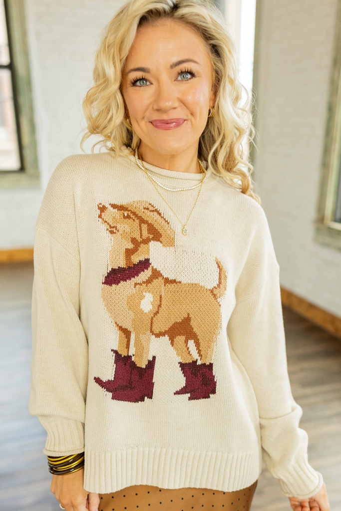 Holly wearing the Western Dog Sweater, a cream pullover sweater with a tan dog wearing a cowboy hat and maroon boots design, paired with a brown polka dot midi skirt.