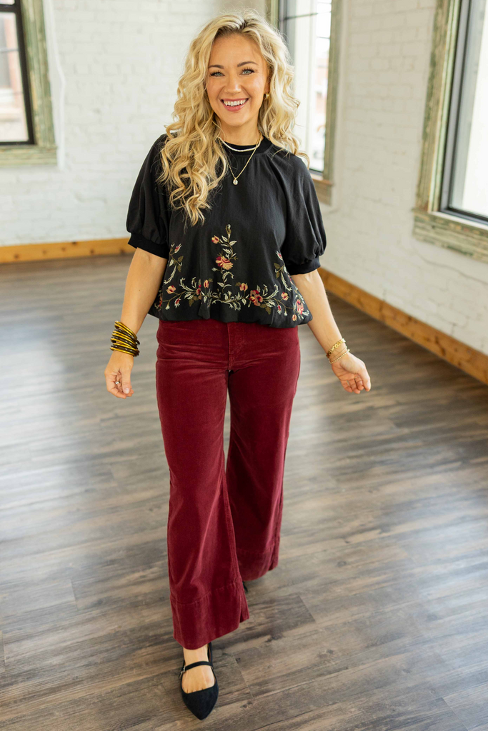 Holly wearing the [RISEN] Winnie High Rise Cropped Corduroy Jeans, wine-maroon cropped wide-leg corduroy pants with a trouser hem, styled with a light gray ringer tee and white sneakers.